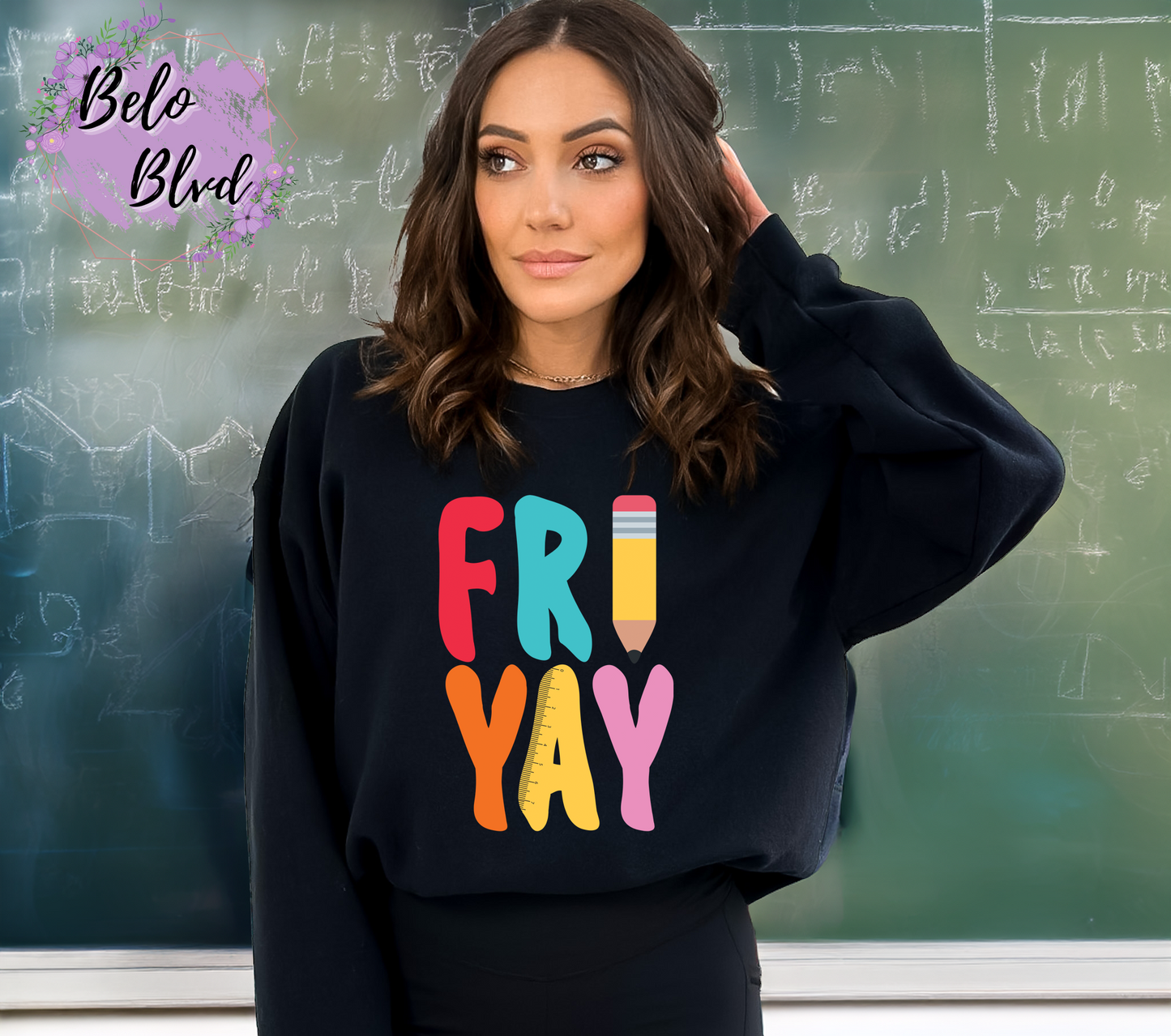 Woman wearing a black crewneck sweatshirt with colorful “FRIYAY” text, including a pencil graphic, standing in front of a chalkboard.