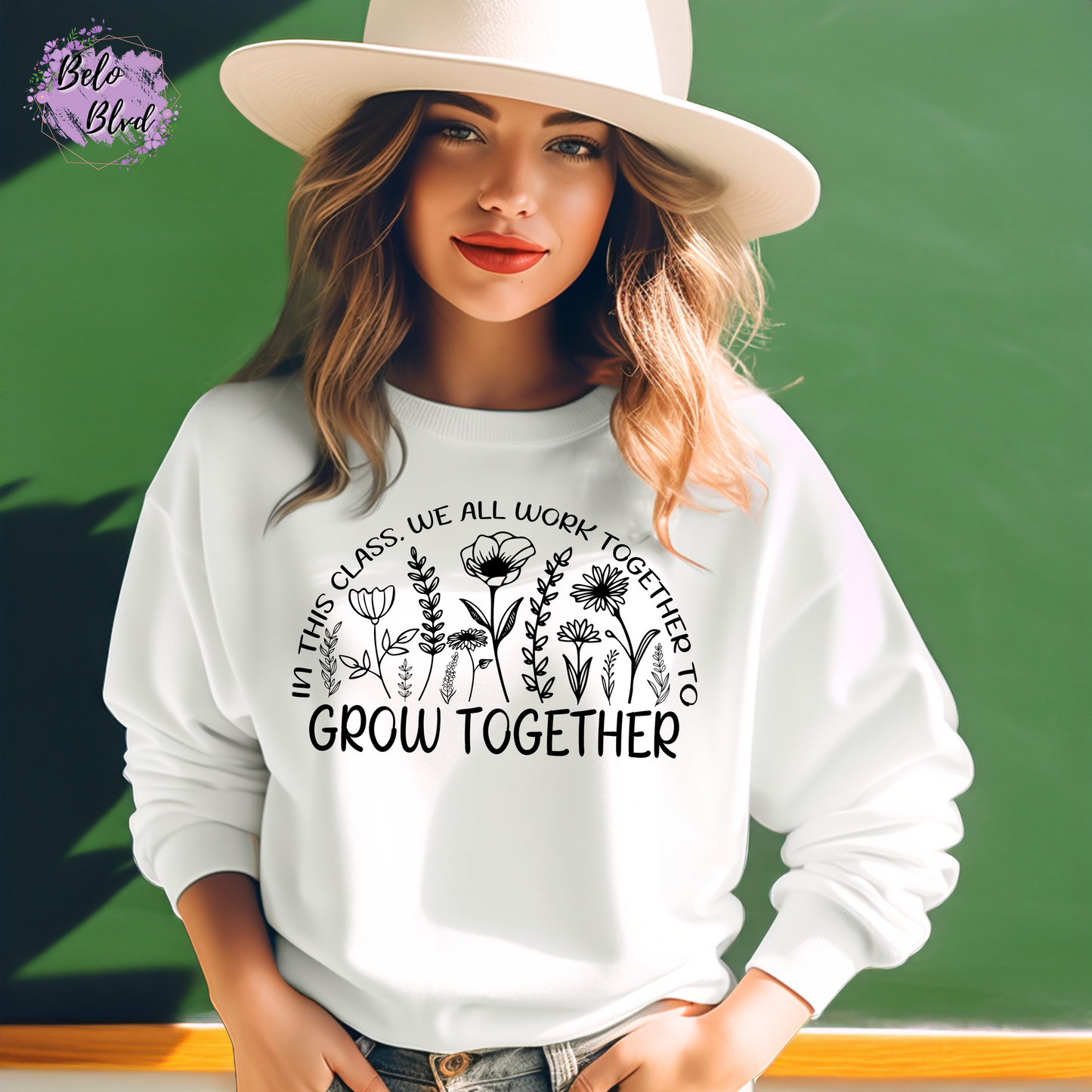 Woman wearing a white crewneck sweatshirt with bold black floral illustration and motivational teacher quote, standing in front of a chalkboard.