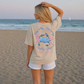 Woman on a beach wearing a t-shirt with a crab graphic and text.