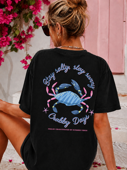 Person wearing a black t-shirt with a blue crab design and text, sitting against a pink floral background.