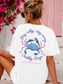 Person wearing a white t-shirt with a blue crab graphic and text, sitting by pink flowers.