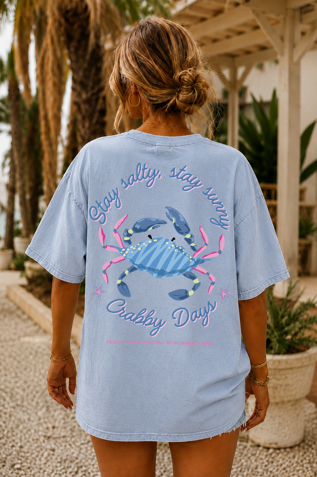 Person wearing a light blue t-shirt with a crab graphic and text, standing outdoors.