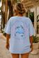 Person wearing a light blue t-shirt with a crab graphic and text, standing outdoors.
