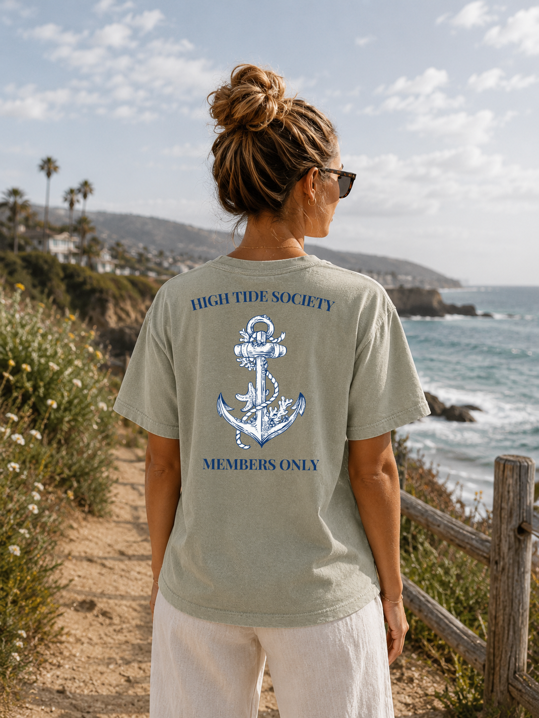 Person wearing a 'High Tide Society' t-shirt with an anchor design by the ocean.