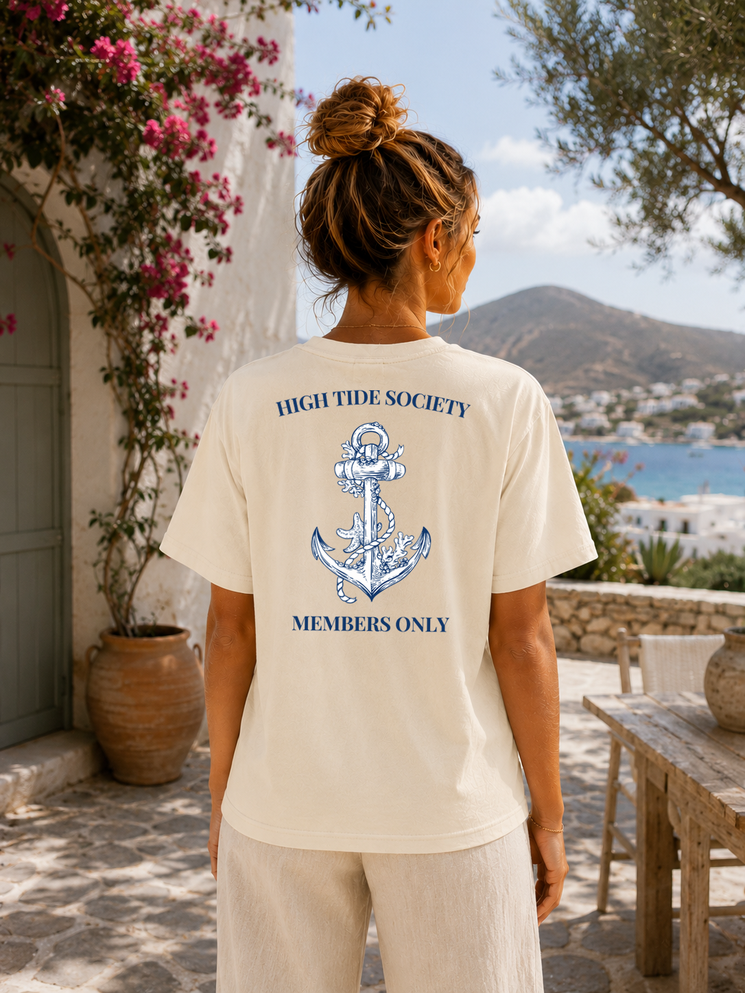 Person wearing a 'High Tide Society' t-shirt with an anchor design, standing in a scenic outdoor setting.