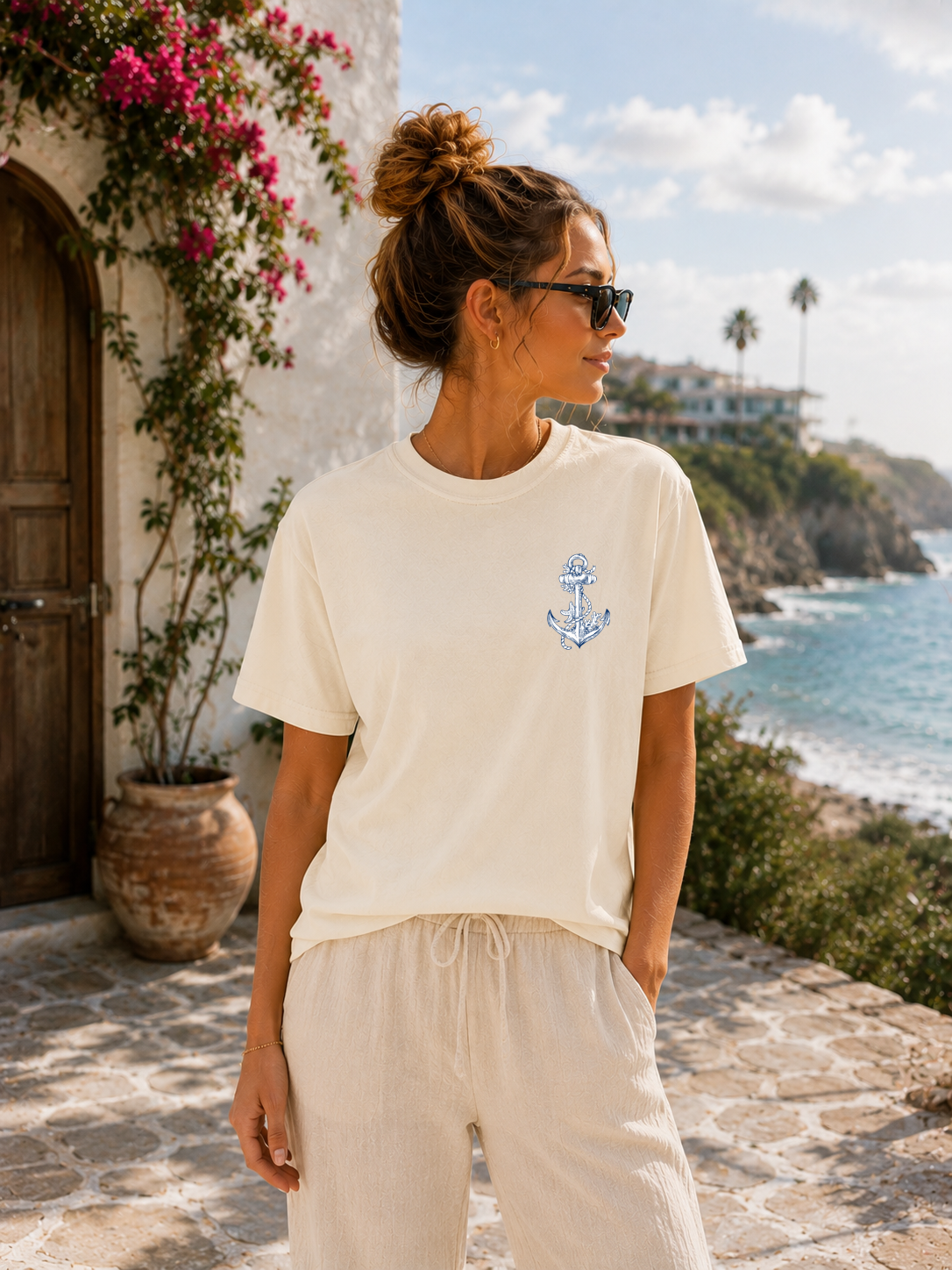 Woman wearing a white t-shirt with an anchor design by a scenic coastal location.