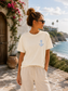 Woman wearing a white t-shirt with an anchor design by a scenic coastal location.
