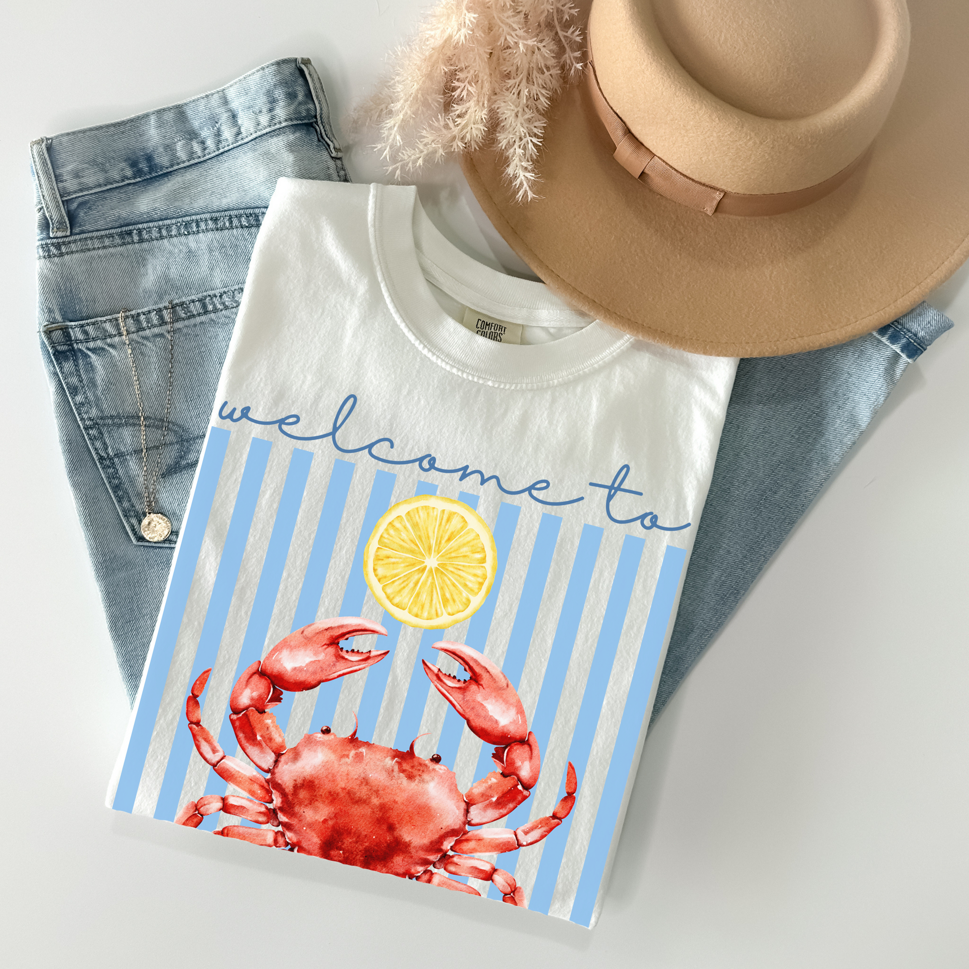 T-shirt with crab and lemon design, placed on jeans and a hat.