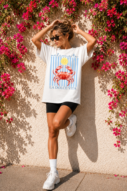 Woman wearing a white t-shirt with a graphic design, standing against a wall with pink flowers.