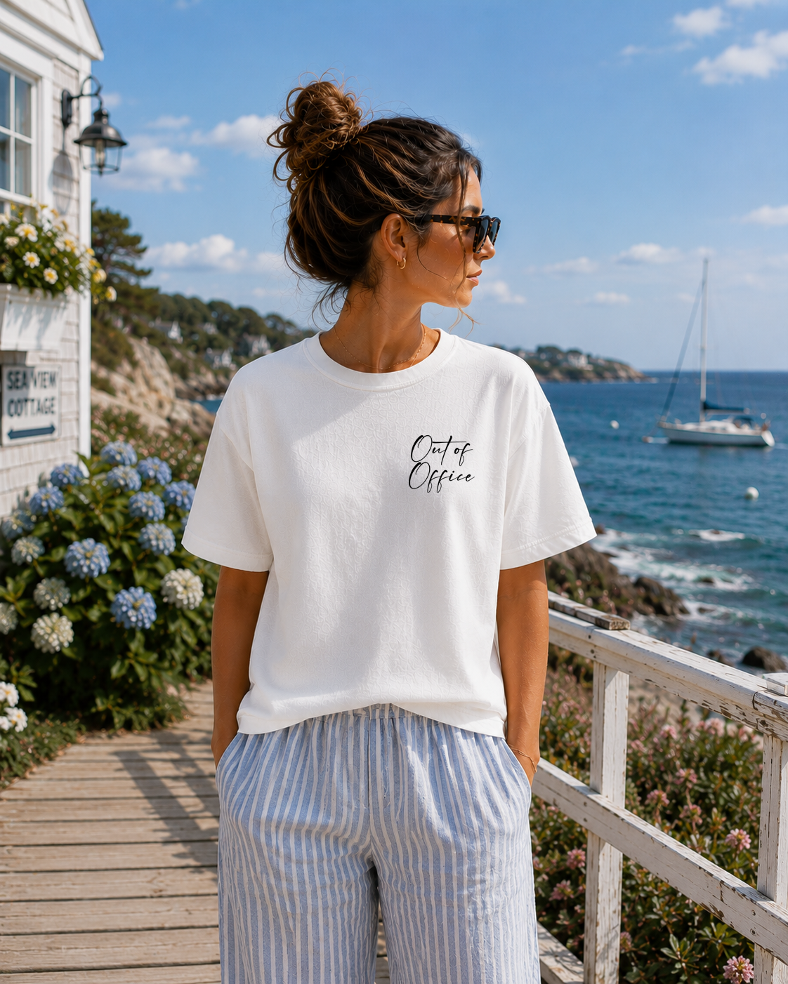 Woman wearing a white t-shirt with 'Out of Office' text by a coastal setting.