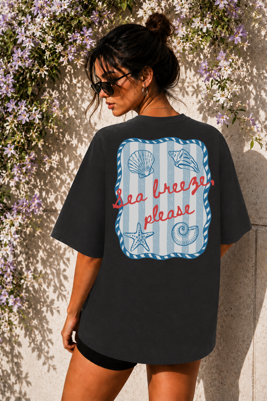 Woman wearing a black t-shirt with a 'Sea Breeze Please' design against a floral wall.