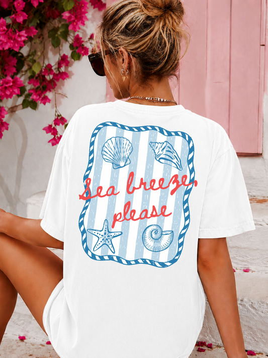 Woman wearing a white t-shirt with beach-themed design and text, sitting by pink flowers.