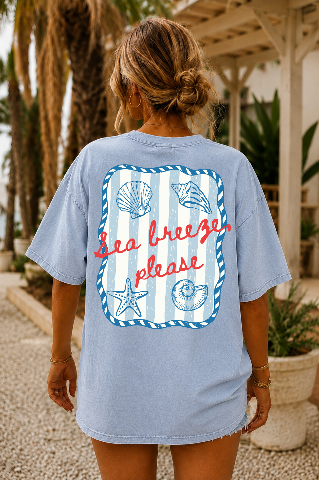 Person wearing a light blue t-shirt with a beach-themed design and text.