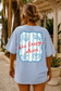 Person wearing a light blue t-shirt with a beach-themed design and text.