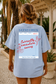 Person wearing a light blue t-shirt with a printed design on the back, standing outdoors.