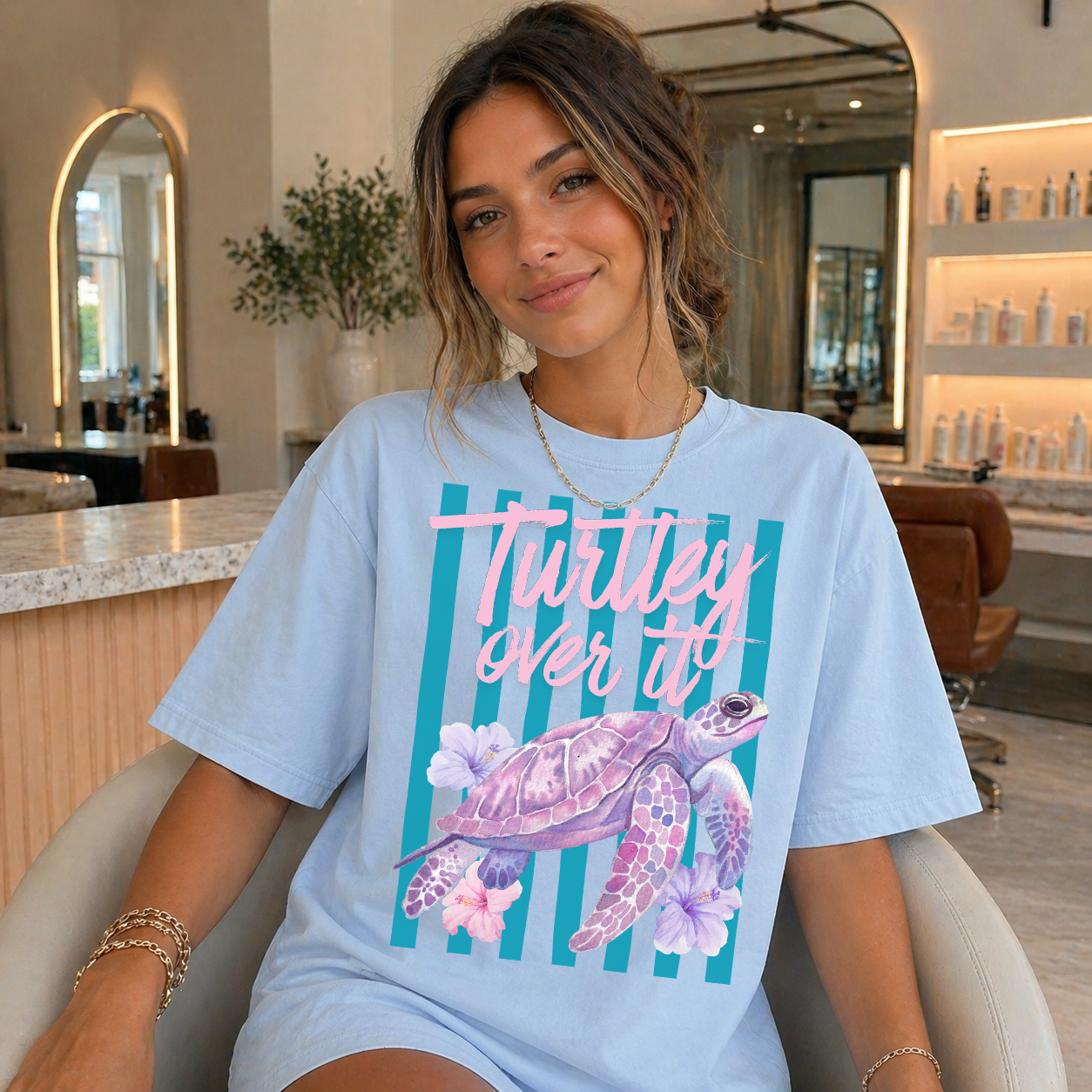Woman wearing a light blue t-shirt with a turtle graphic and 'Turtles over it' text in a salon setting.