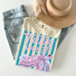 T-shirt with a turtle design and text, placed on denim jeans and a beige hat.