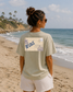 Woman on a beach wearing a t-shirt with a graphic design.
