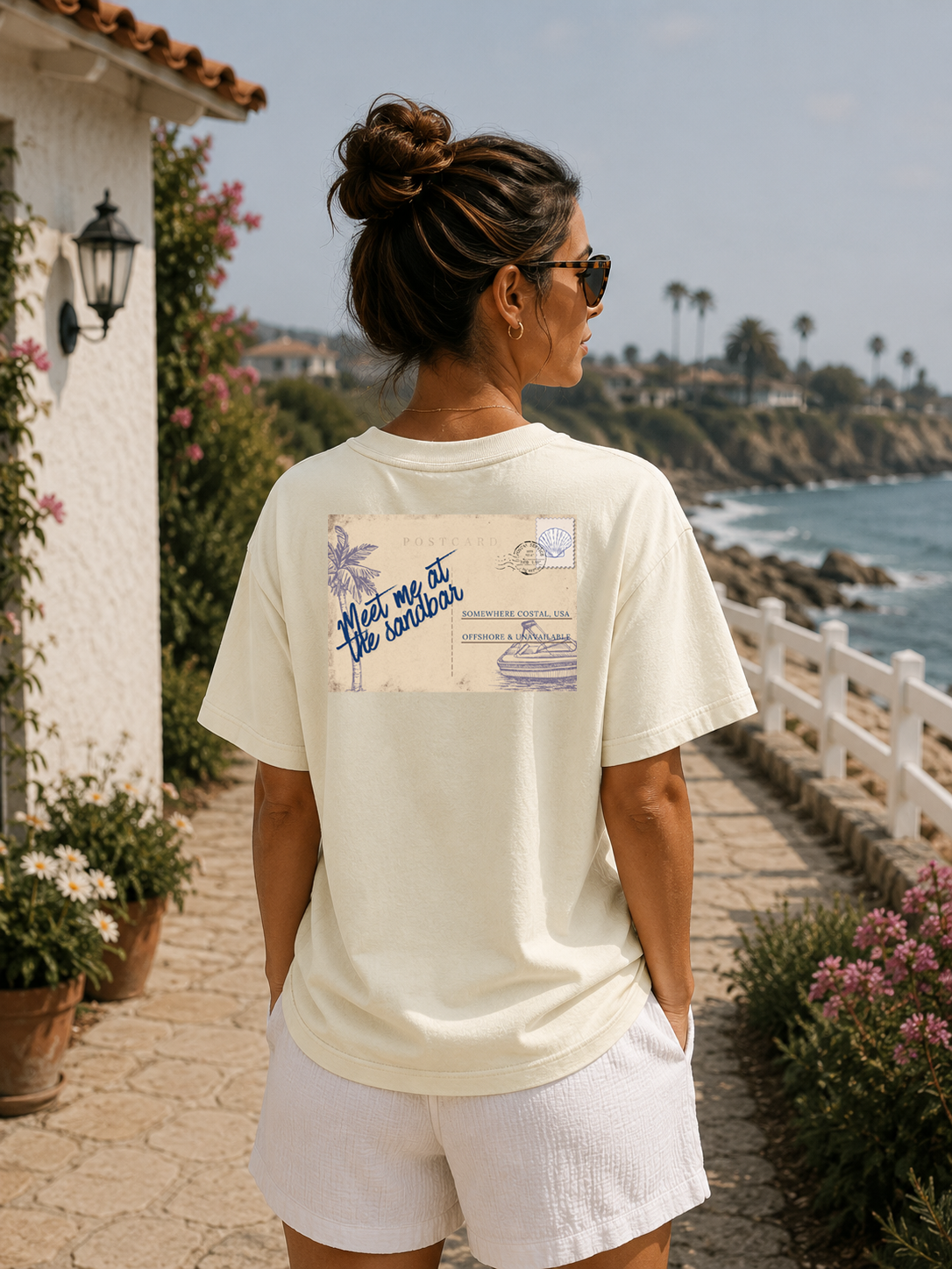 Woman wearing a white t-shirt with a graphic design, standing by a scenic coastal path.