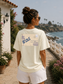 Woman wearing a white t-shirt with a graphic design, standing by a scenic coastal path.